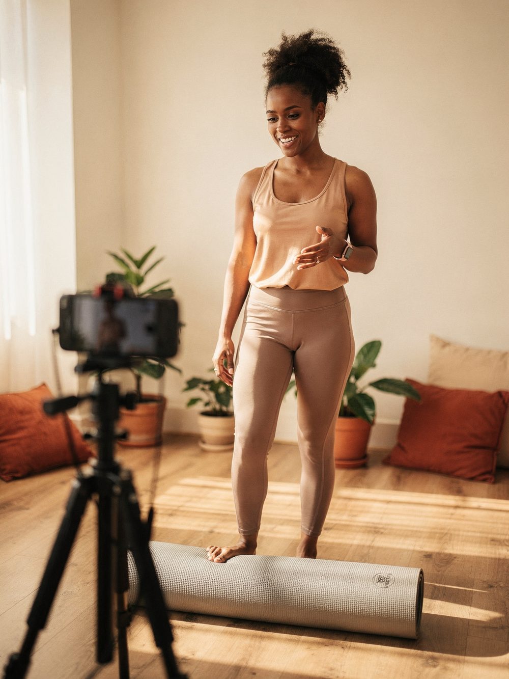 Personal trainer gravando uma aula com o celular no tripé, em um estúdio pequeno e iluminado